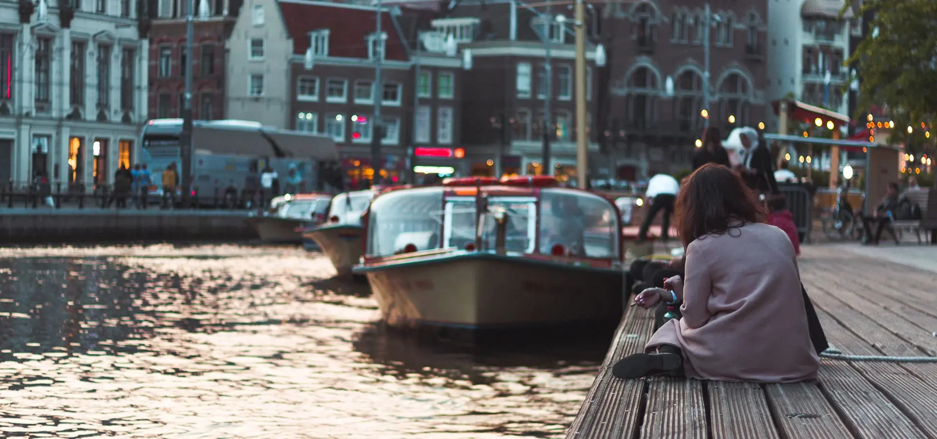 Canal with a boat in the Netherlands and an expat woman sitting on the embankment
