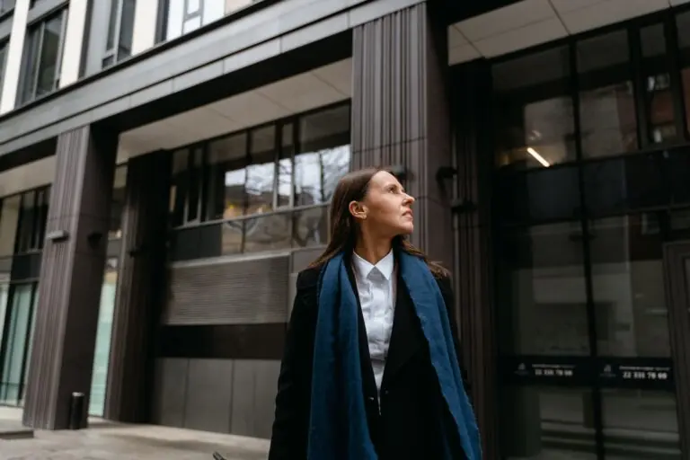 A professional woman in a coat looking up at a modern European city building, considering a career move to Europe