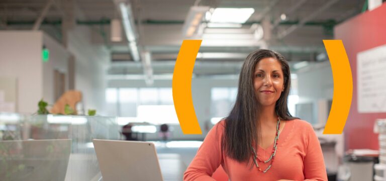 Smiling professional woman standing at an office desk with a laptop